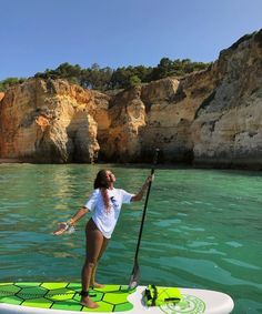 a woman is standing on a surfboard in the water with a paddle and paddling gear