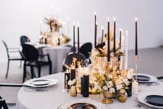 the table is set with black and white plates, silver napkins, gold rimmed candles and floral centerpieces