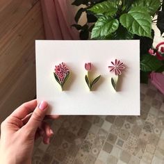 a person holding up a card with two flowers on it and one flower in the middle