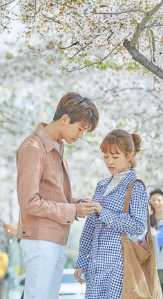 two people standing under a tree looking at their cell phones