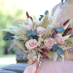 a bridesmaid holding a bouquet of flowers and feathers in her hand, outdoors