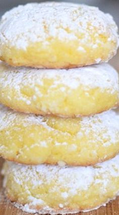 a stack of three lemon filled donuts on top of a wooden table with powdered sugar