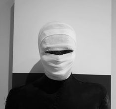 a person with a white mask on their face and black hair in front of a wall