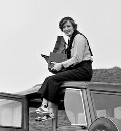 a woman sitting on the roof of a car holding a paper bag in her hand