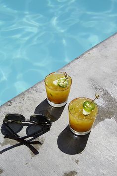 two glasses sitting on the edge of a swimming pool next to a pair of sunglasses