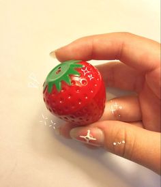 a hand holding a small red strawberry with green leaves on it