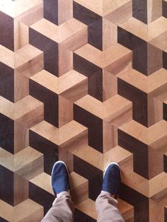 a person standing on top of a wooden floor next to a wall with geometric designs