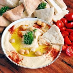 hummus, pita bread and tomatoes on a wooden table with other food items