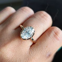 a woman's hand with a ring on it that has an oval shaped diamond in the center