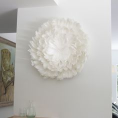 a large white flower hanging on the wall next to a table with vases and bottles