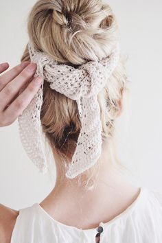 a woman with her hair in a bun wearing a white scarf around her neck and hands on the top of her head