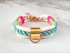 a white and blue bracelet with gold clasps on a marble counter top next to a key