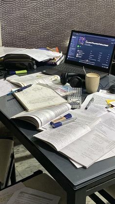 a laptop computer sitting on top of a desk covered in papers and paperwork next to a cup of coffee