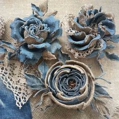 three blue flowers with lace on them sitting on a piece of burlied fabric