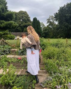 a woman holding a child in her arms while walking up steps into a vegetable garden