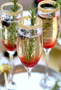 three glasses filled with liquid and garnish sitting on top of a silver tray