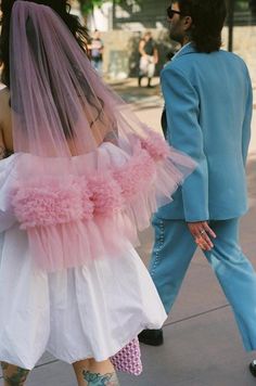 a man and woman walking down the street wearing wedding dresses with pink flowers on them