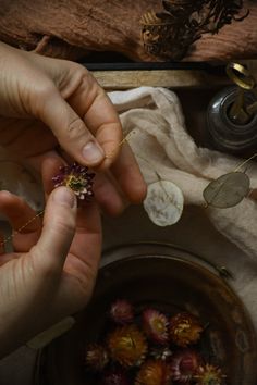 two hands are holding flowers in front of a bowl with petals on the table next to it