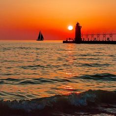 the sun is setting over the ocean with a sailboat in the water below it