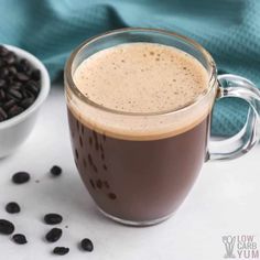 a glass mug filled with coffee next to a bowl of beans and a blue towel