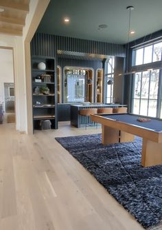 a pool table in the middle of a living room with large windows and wooden floors