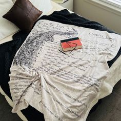 a blanket that is laying on top of a bed next to a book and pillow