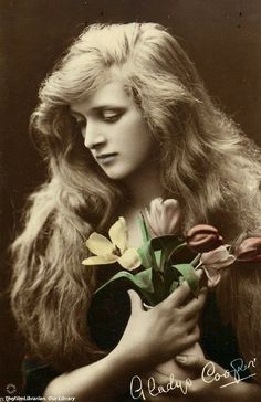 an old black and white photo of a woman with long hair holding flowers in her hands