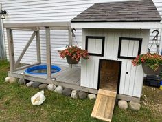 there is a chicken house with flowers in the window and on the ground next to it