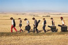 a group of people walking across a dry grass field with suitcases in their hands