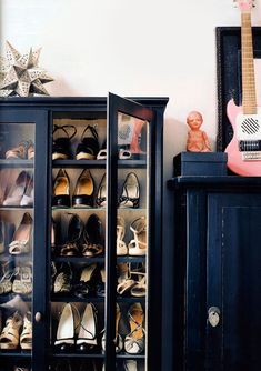 a black cabinet filled with shoes next to a guitar and other items on top of a table