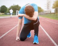 a man kneeling down on a track with his head in his hands while wearing blue shoes