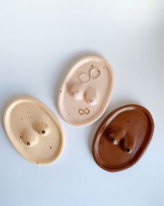 three ceramic bowls with holes in them on a white surface, one is brown and the other two are beige