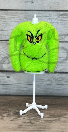 a green sweater with yellow eyes on a white stand