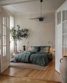 a bed sitting in a bedroom next to a plant on top of a wooden floor