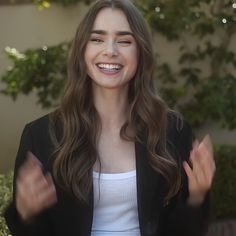 a woman with long hair is smiling and holding her hands out in front of her