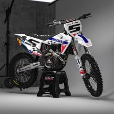 a white and blue dirt bike sitting on top of a black stand in front of a gray wall