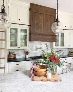 a kitchen with white cabinets and marble counter tops, two hanging lights above the sink