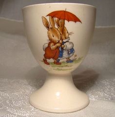 a ceramic egg cup with a rabbit holding an umbrella on it's side, sitting on a white tablecloth