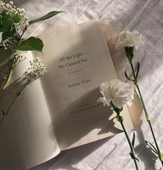 an open book sitting on top of a bed next to white flowers and greenery