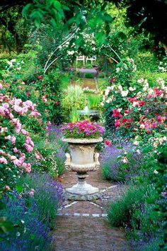 a garden filled with lots of flowers next to a stone path through a lush green forest