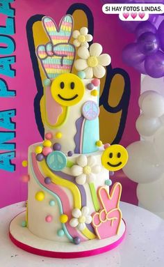 a multi - tiered cake decorated with flowers and smiley faces on a table in front of balloons