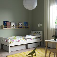 a child's room with a bed, desk and toy dinosaur on the floor