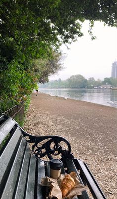 a cup of coffee and some croissants on a bench by the water