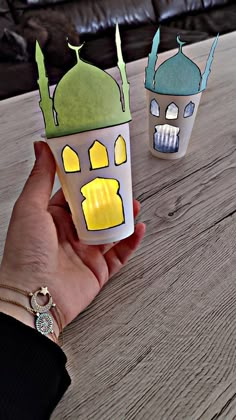 a hand is holding two cups that have designs on them, one with a green roof and the other with a blue dome