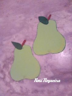 two pears with green leaves cut out of them on a purple surface, one is yellow and the other is green