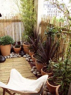 an outdoor patio with potted plants and rocks on the floor, along with a bamboo fence