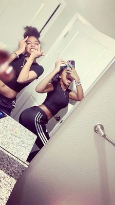 two young women standing in front of a bathroom mirror taking selfies with their cell phones