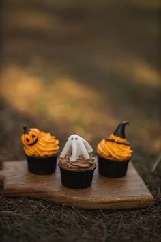 three halloween cupcakes with chocolate frosting and ghost decorations on top, sitting in the grass