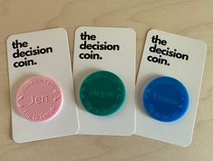 three different colored buttons sitting on top of a white card that says the decision coin