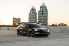 a black tesla model 3 parked in front of some tall buildings with skyscrapers behind it